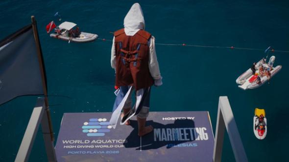 Tuffatore si lancia da scogliera rocciosa verso il mare blu in una manovra acrobatica